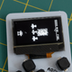 A close-up of the Arduboy Mini's OLED screen showing a 1942-style game being played.